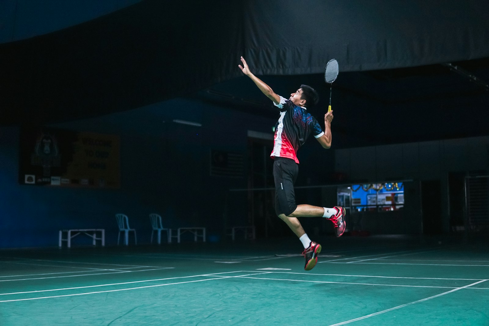 Badminton player mid-air winding up a jump smash on an indoor court