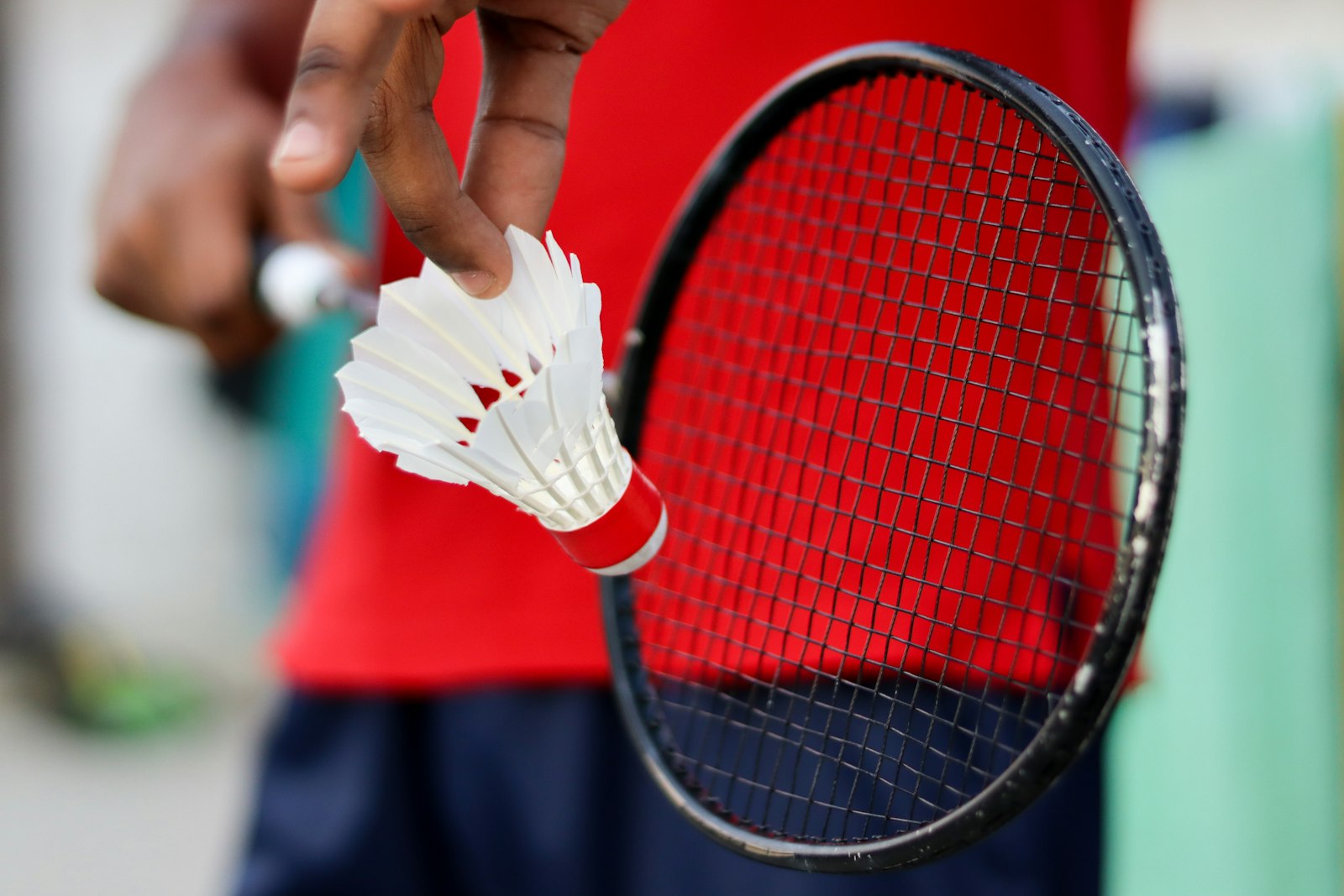 Hand holding a feather shuttlecock in front of a badminton racket
