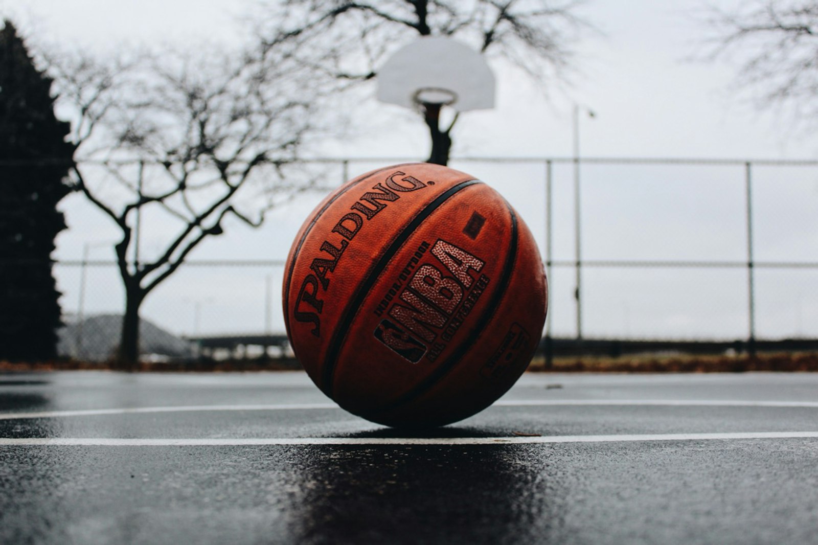 Weathered basketball resting on a wet outdoor court in front of a hoop