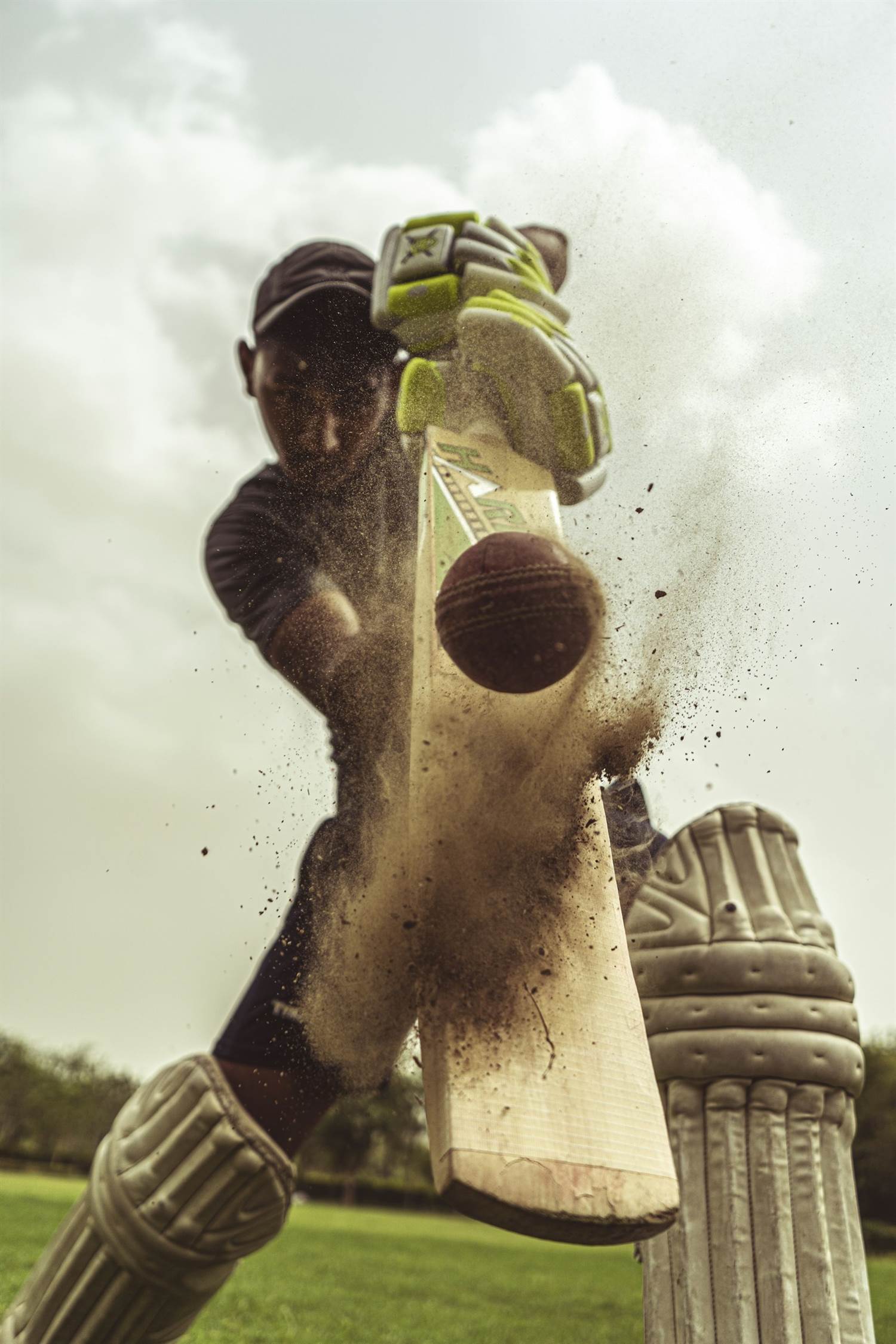 Batter striking a cricket ball in a cloud of dust, viewed from the stumps