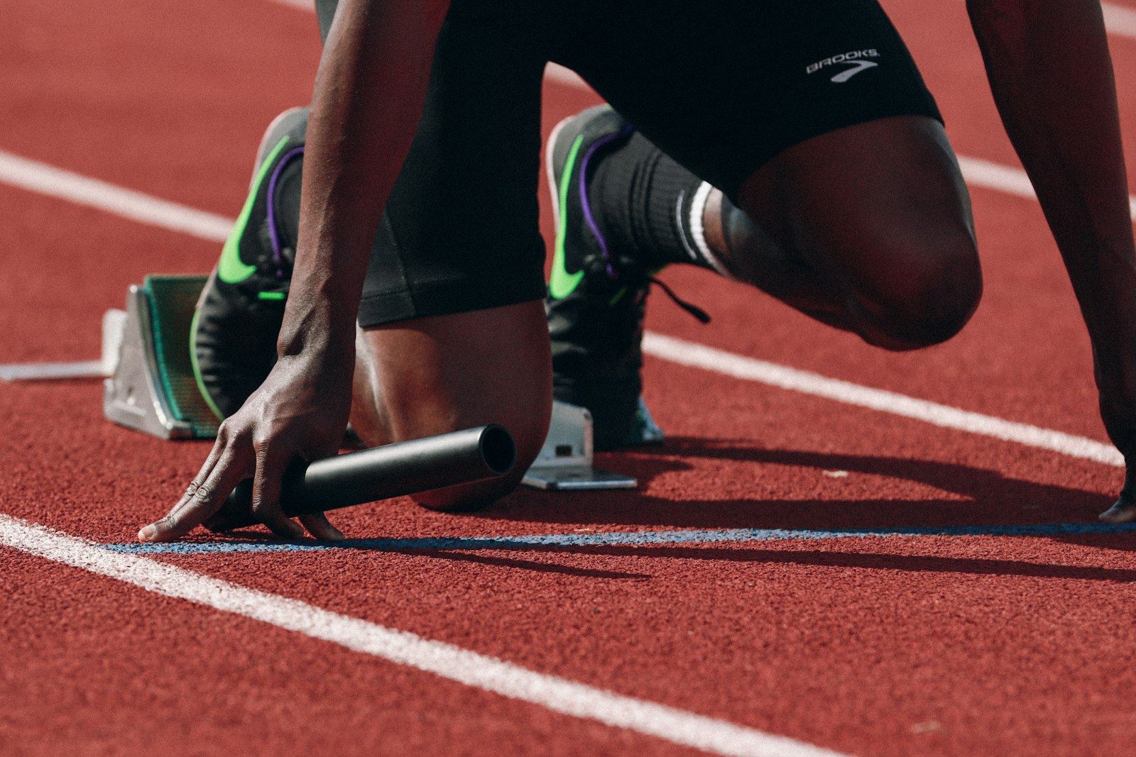 Sprinter crouched in the starting blocks holding a relay baton