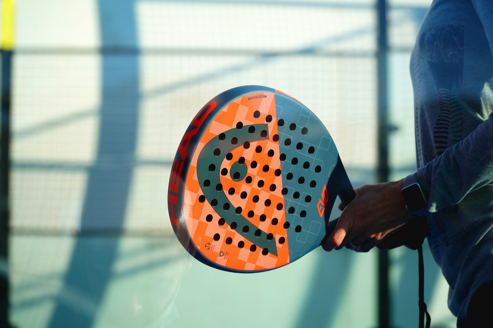 Player holding an orange padel racket in front of a court