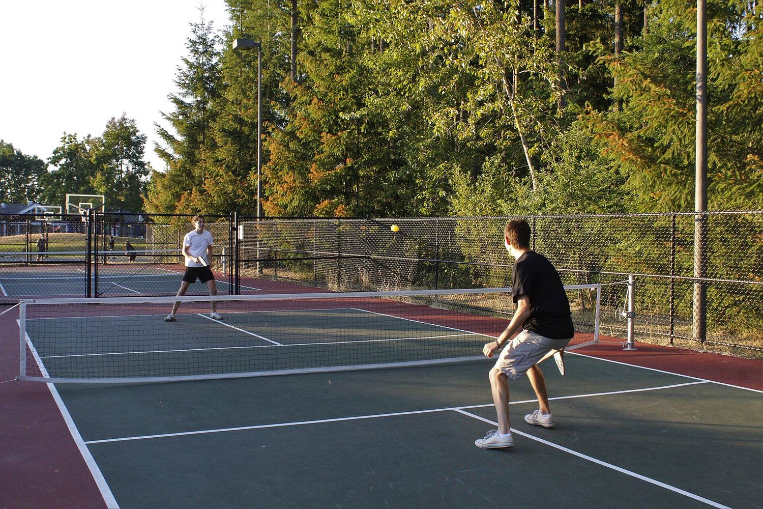 Two players rallying on an outdoor pickleball court with the yellow ball in mid-air