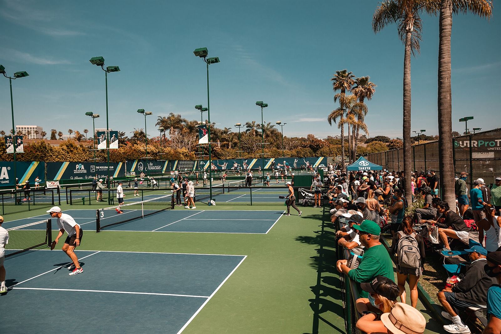 Outdoor pickleball tournament with multiple blue courts and spectators