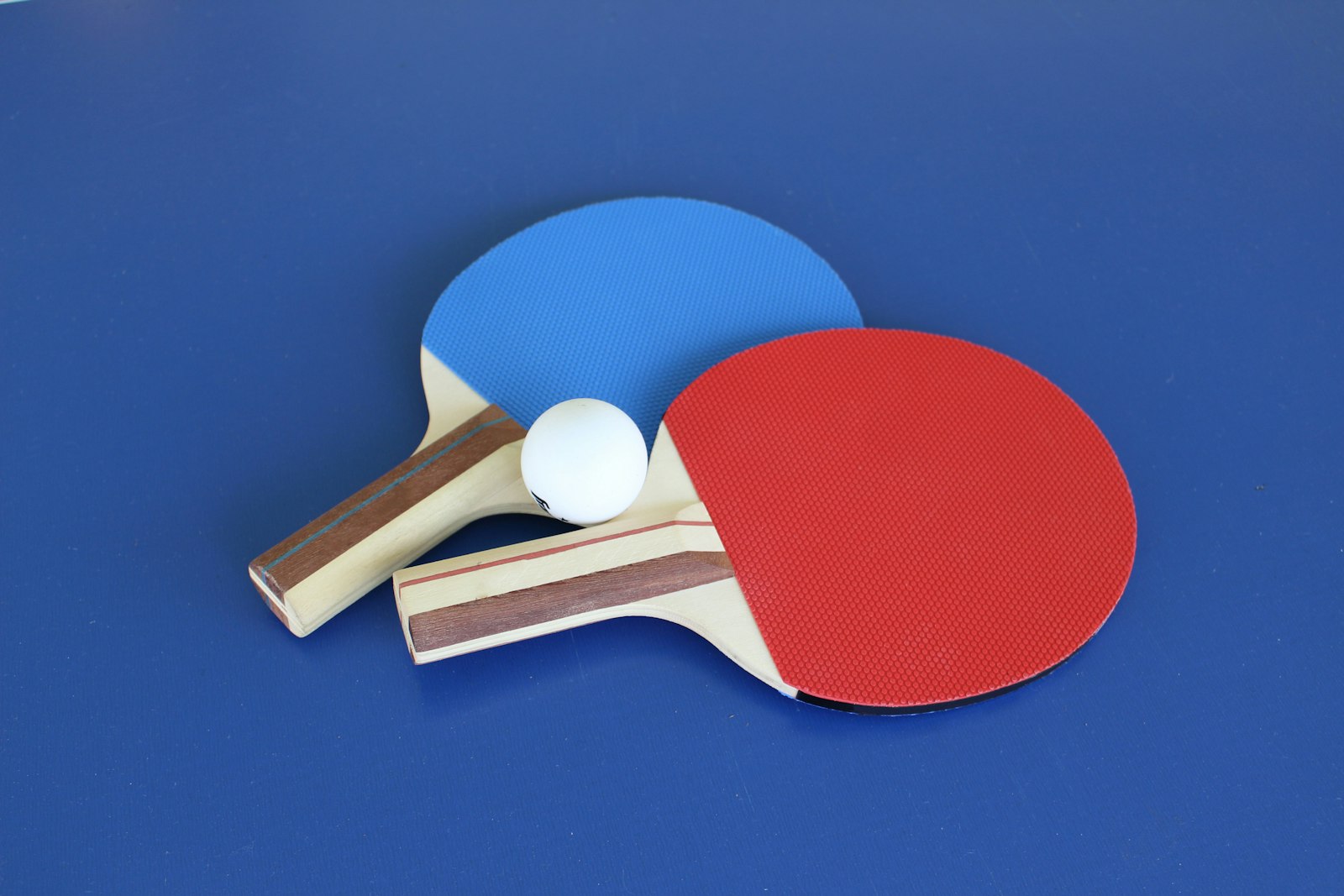 Red and blue table tennis paddles with a ball on a blue table