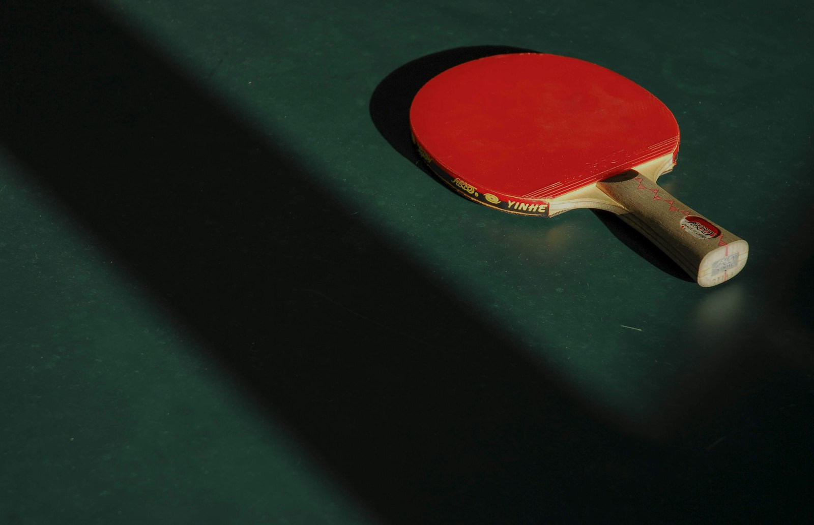Red table tennis paddle lying in dramatic light on a dark table